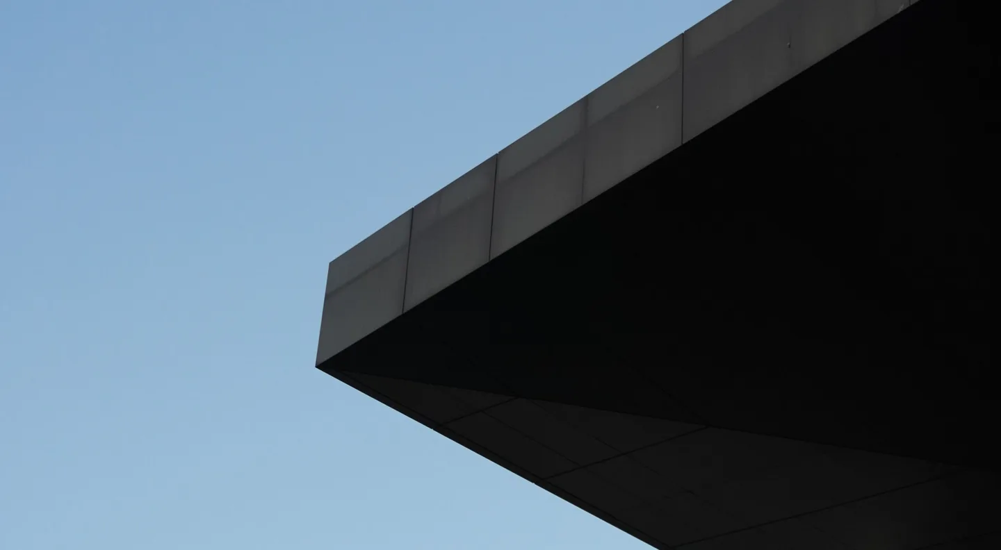 A dark cantilevered roof cutting across a pale blue sky.