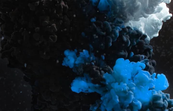 Blue and white ink blooming through dark water.