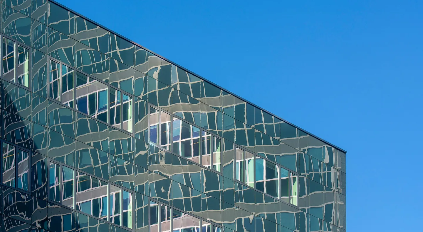 A rippled glass facade holding its reflections, cut against a clear blue sky.